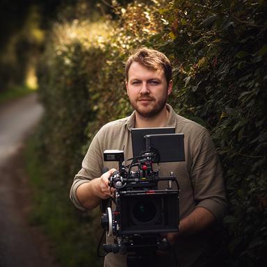 Devon videographer holding a cinema camera beside a hedgerow on Peek Lane