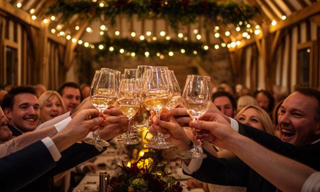 Wedding guests raising glasses inside a decorated Devon barn during an evening reception